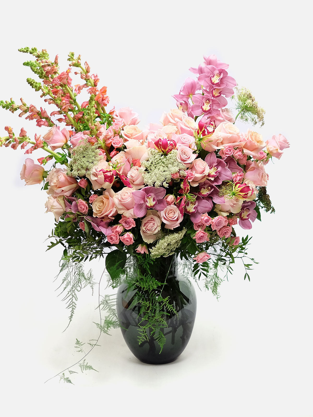 A heart-shaped floral arrangement with shades of pink and peach flowers, along with greenery, in a clear vase.
