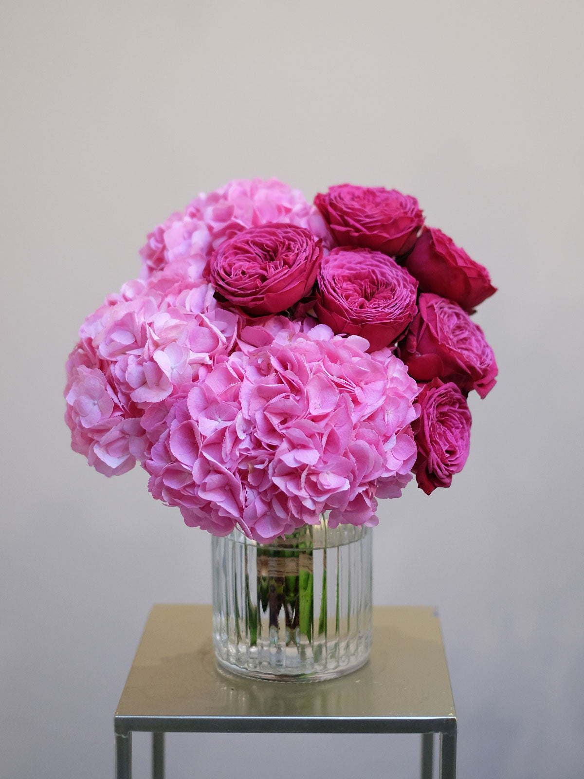 A floral arrangement of pink hydrangeas and garden roses in a clear glass vase, placed on a table.