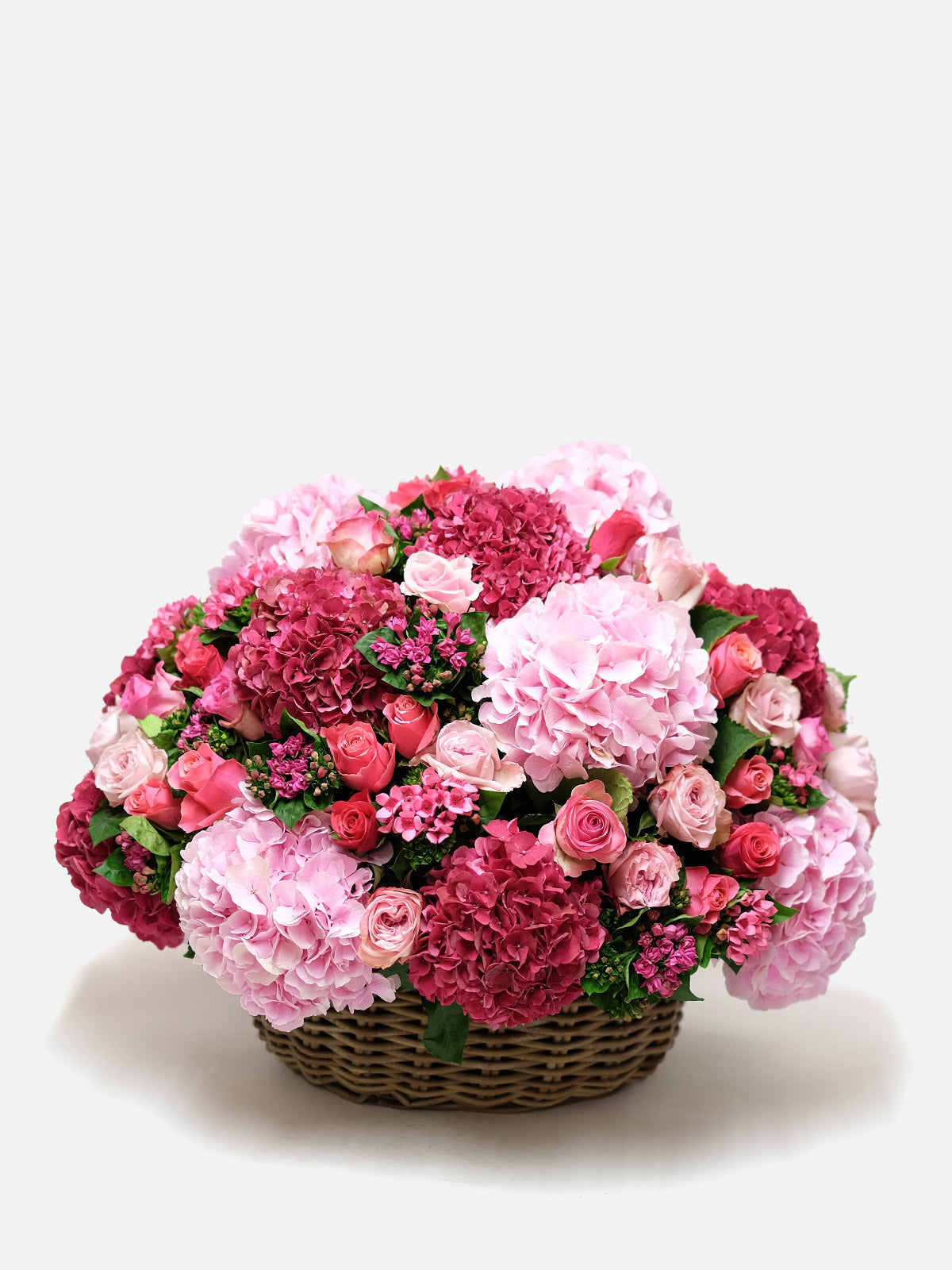 A beautifully arranged pink floral symphony composed of various pink flowers, placed in a wicker basket against a white background.