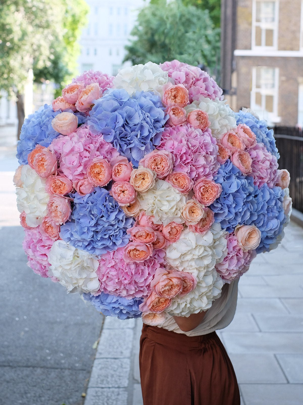 Person holding a large bouquet of colorful flowers in an urban setting